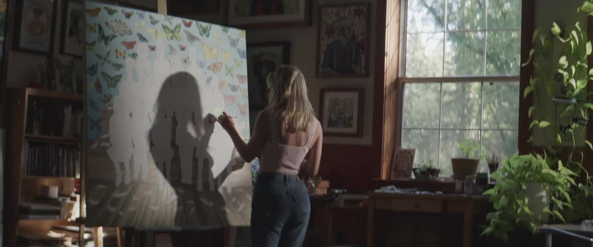 Blonde female paints on large canvas indoors near window
