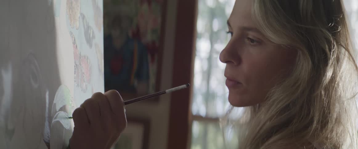 A blonde white woman paints on a canvas