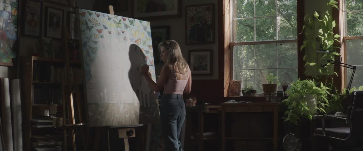 Female artist stands painting large canvas while standing in an art studio