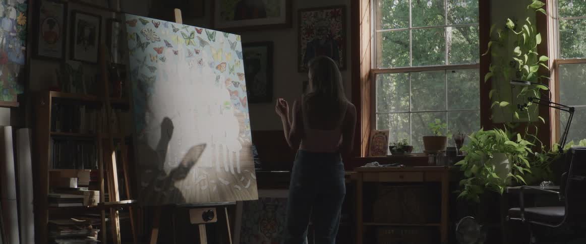 Blonde woman paints canvas on easel indoors near window