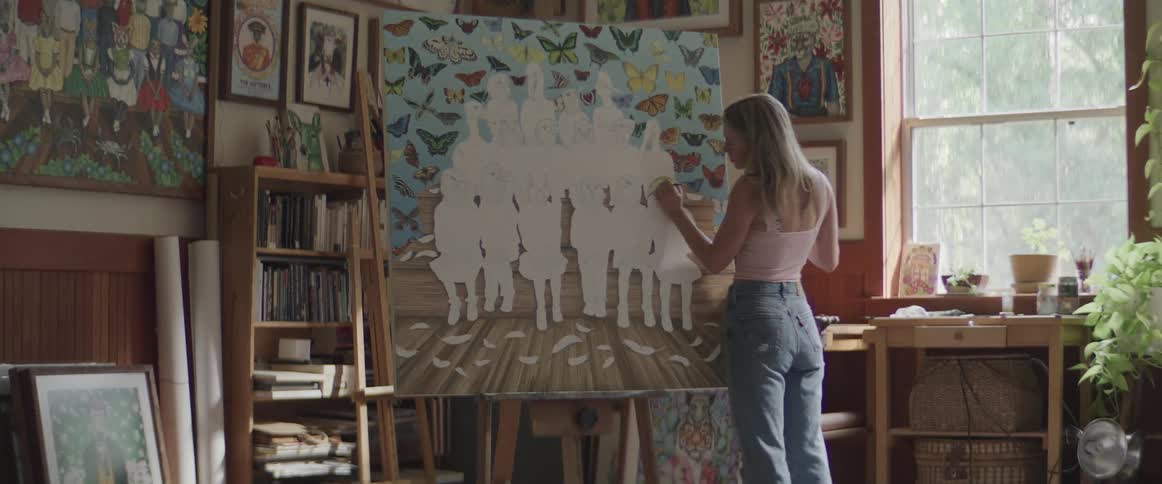 A blonde woman paints on a large canvas