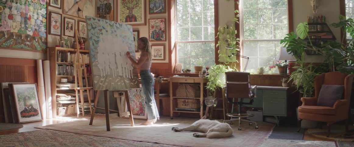 A woman painting on a canvas with a dog lying on the floor sleeping