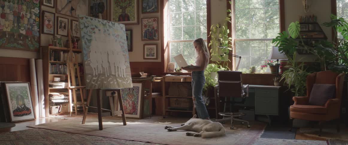Woman working on her notebook in a room with a painting and her dog next to her sleeping on the floor