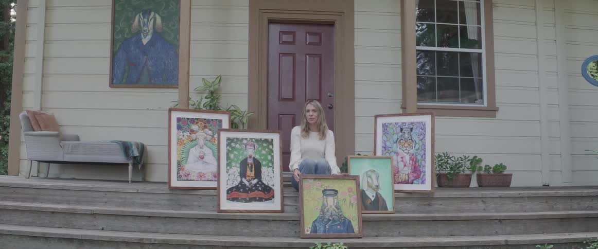 Blonde woman sits on steps in front of house with framed artwork