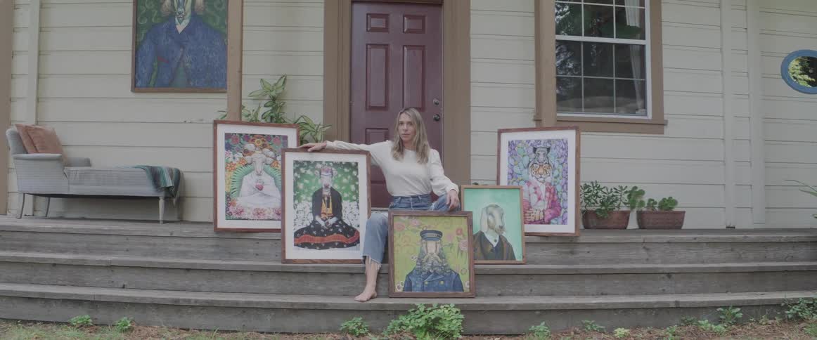A woman is sitting on the steps with her paintings on display