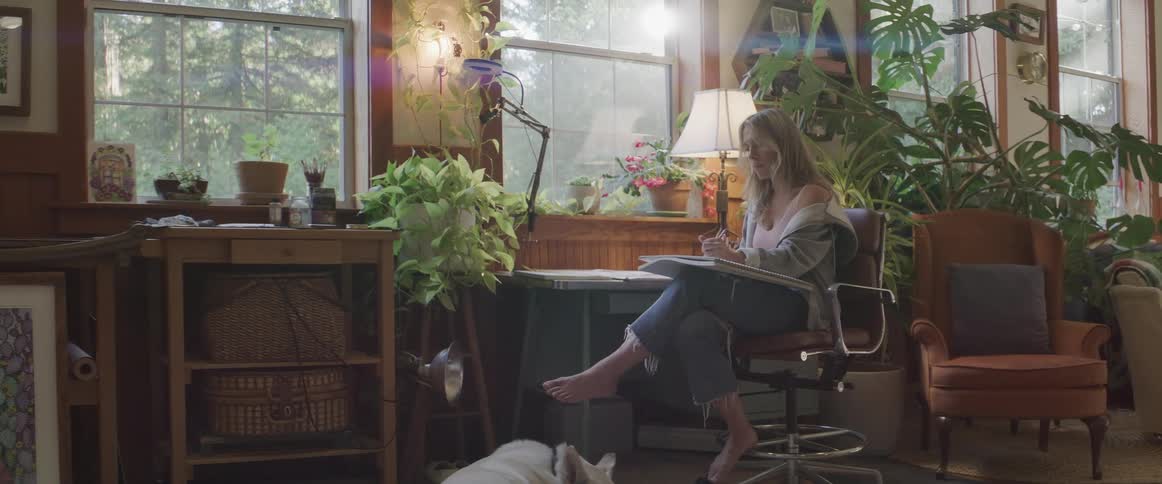 A white woman sits in a chair and draws on a pad
