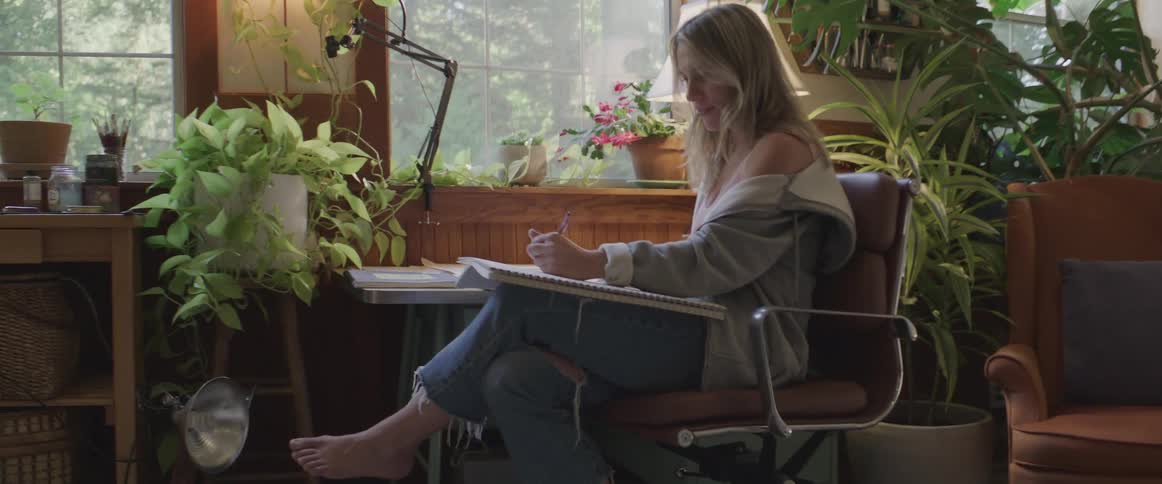 Woman sitting on a chair in a room with bushes and writing in a notebook