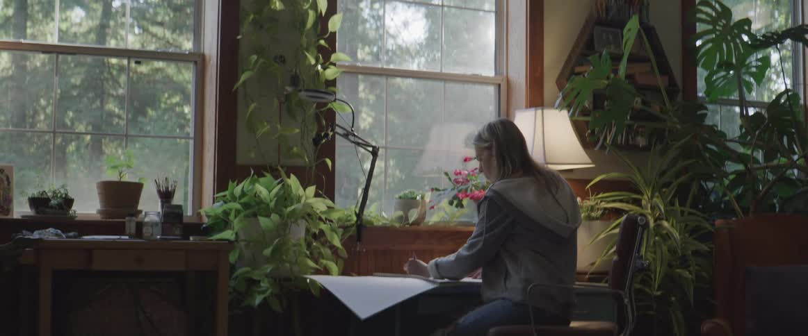 Female sits at desk near window and sketches on paper