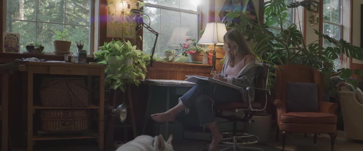A woman draws while a dog sleeps at her feet
