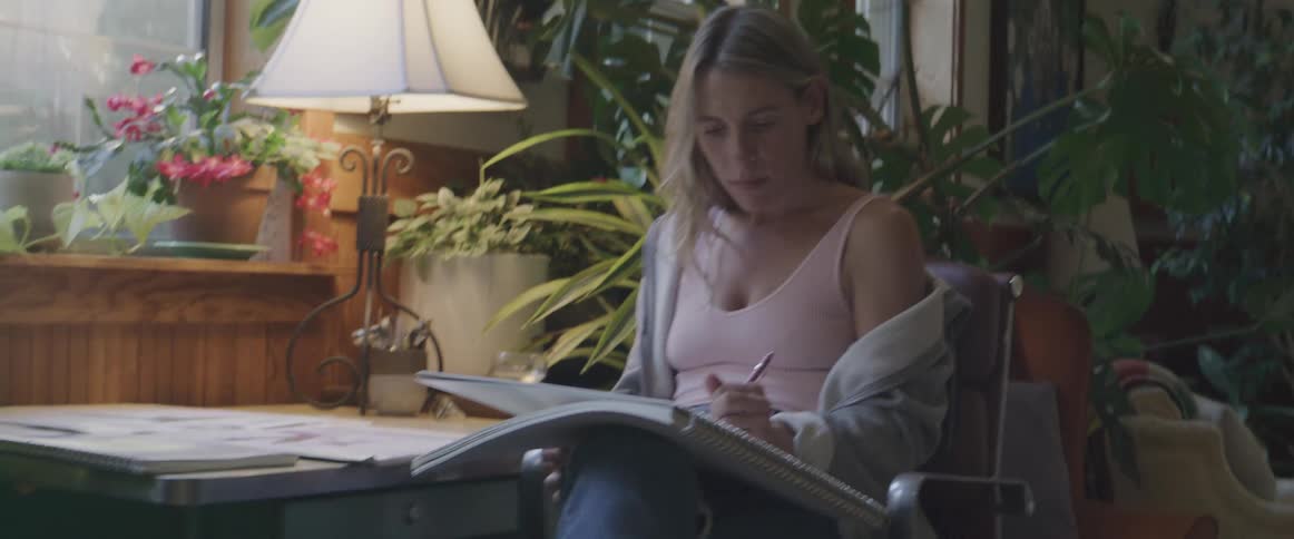 A concentrated woman drawing in a notebook in the living room