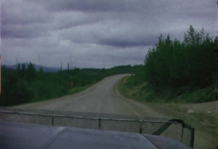 A car is driving down a dirt road in a wooded area
