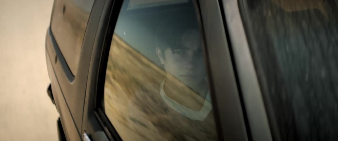 A young boy sitting in a car looking out the window that is reflecting a desert environment