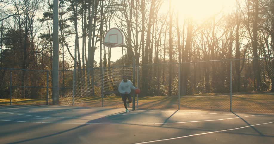 Man wearing a hoodie practices basketball on a park at morning