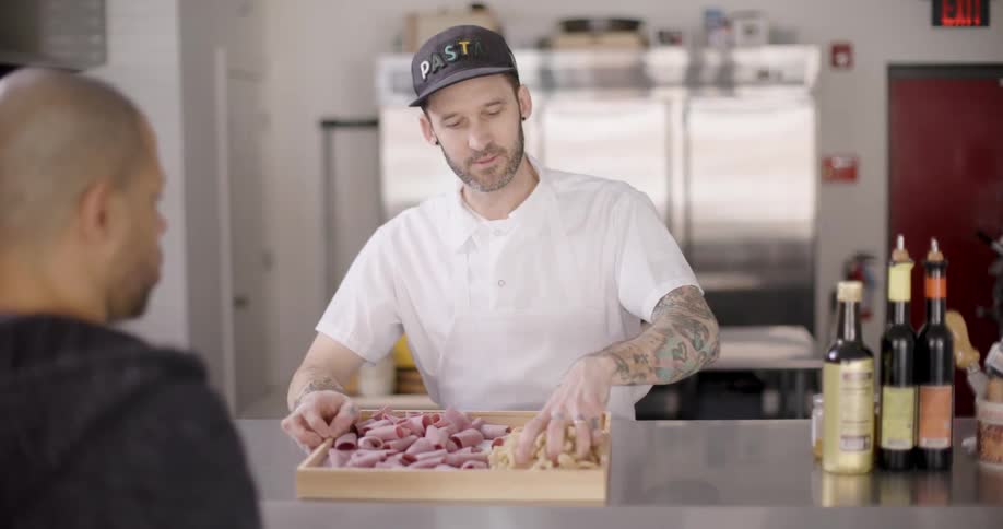 Man presenting pasta and ham to a customer at the counter