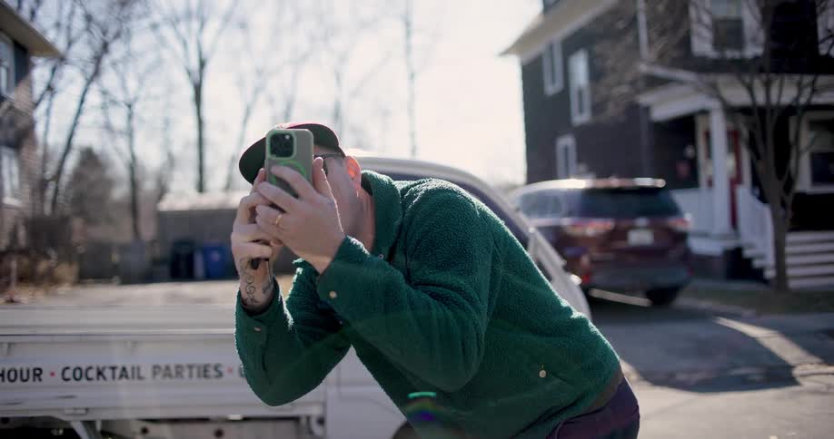 Man takes picture with smartphone near restaurant owned vehicle parked in residential area
