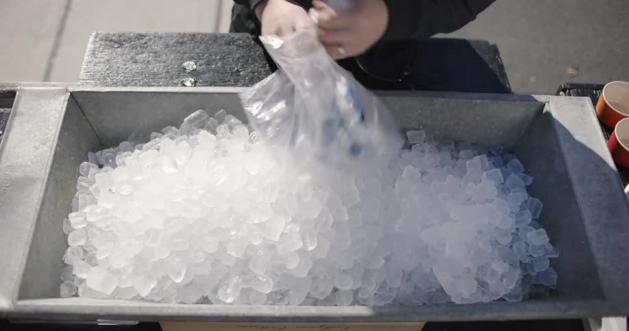 Arms of a person pouring ice into a metal bucket