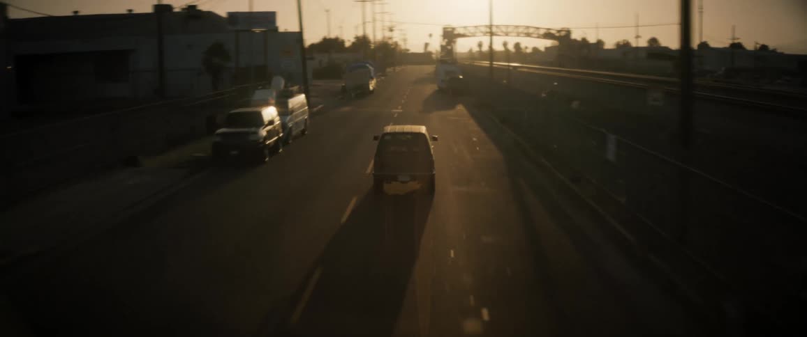 A car is driving on a road in the industrial sector of a town during sunset