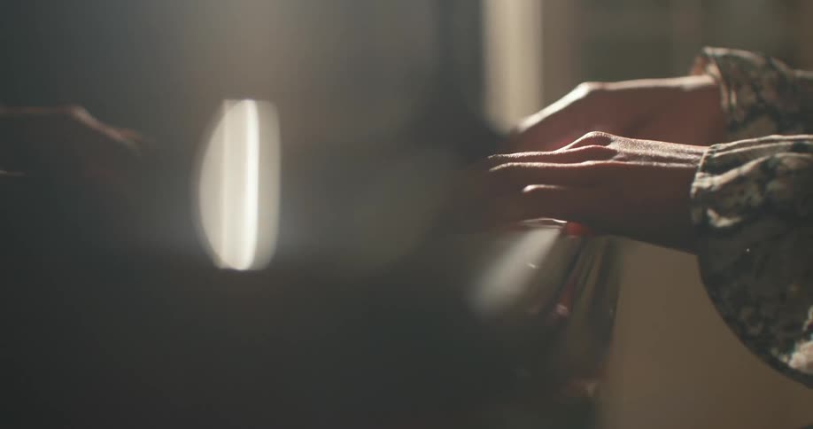 A person plays a piano in a dimly lit room wearing a ruffled blouse
