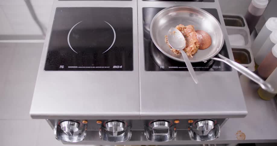 A man with multiple tattoos stirs some food in a pan as he cooks it