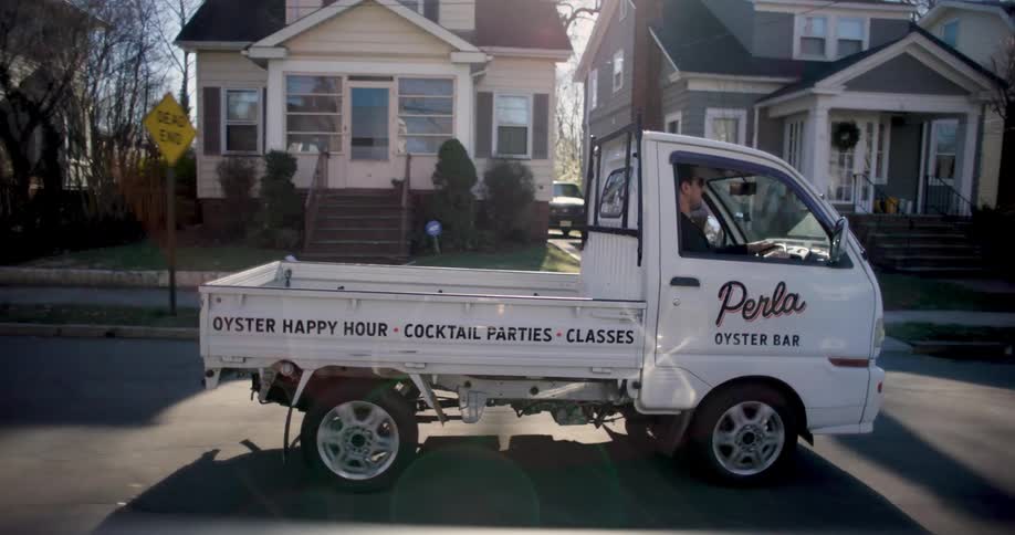 Two men drive a small truck through a residential neighborhood