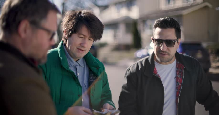Three standing men are looking down and a man wearing sunglasses is talking to the man in front of him