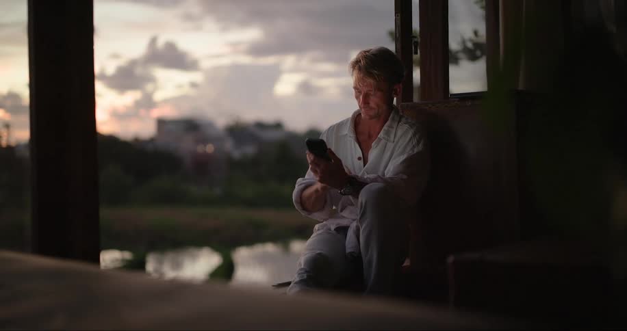 Man sitting in the patio at sunset looking at his phone