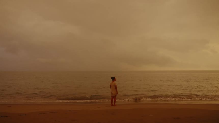 A young Asian woman by the sea during a dramatic and cloudy sunset