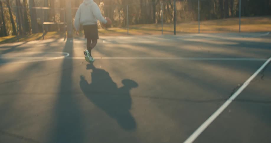 A man playing basketball on an outdoor court in the morning