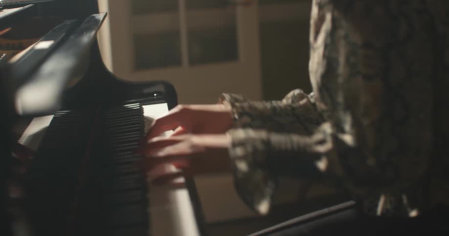 A woman seated in a small room plays music on a grand piano