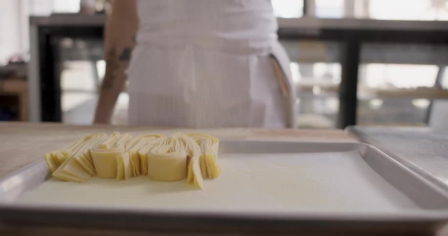 Chef sprinkling flour over fettuccine noodle on a cookie sheet