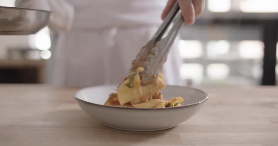 A person serving noodles on a porcelain plate