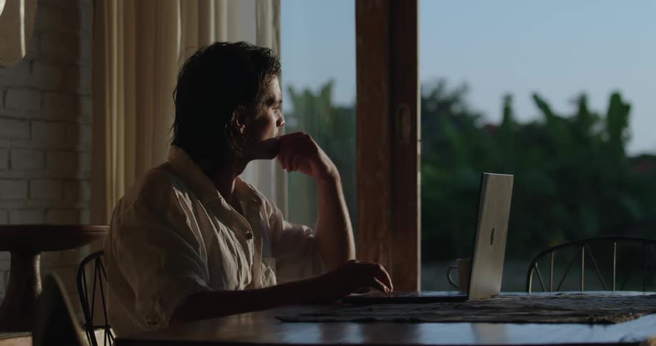 Man in a white shirt sits at table works on laptop