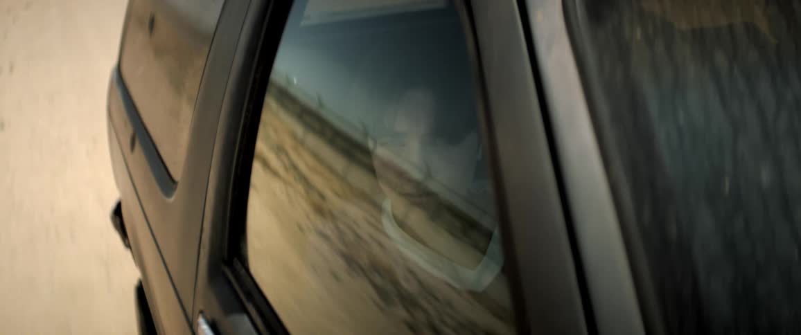 Male passenger stares out car window reflecting the rural countryside during a road trip