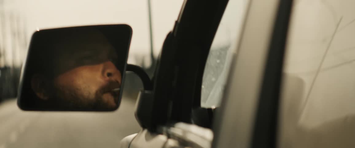 Side mirror reflects driver lighting a cigarette while driving
