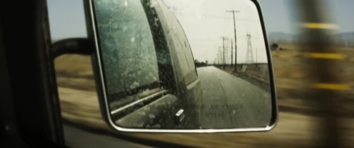 Utility poles pass by in the sideview mirror on a drive down a country road