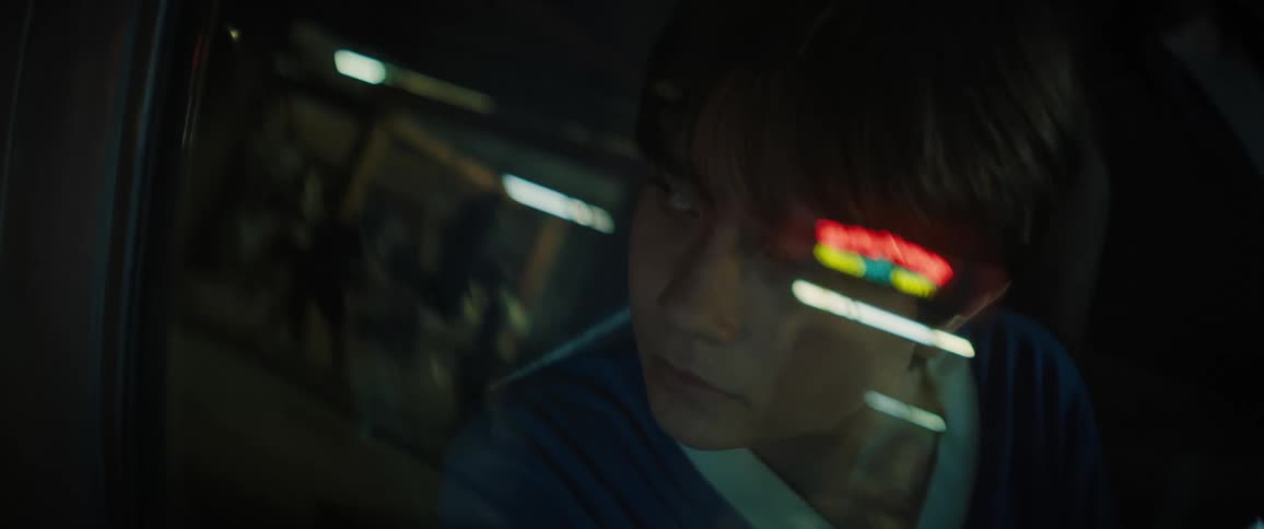 A teenage boy in a car is looking out the window at the reflection of people and then looks to his side