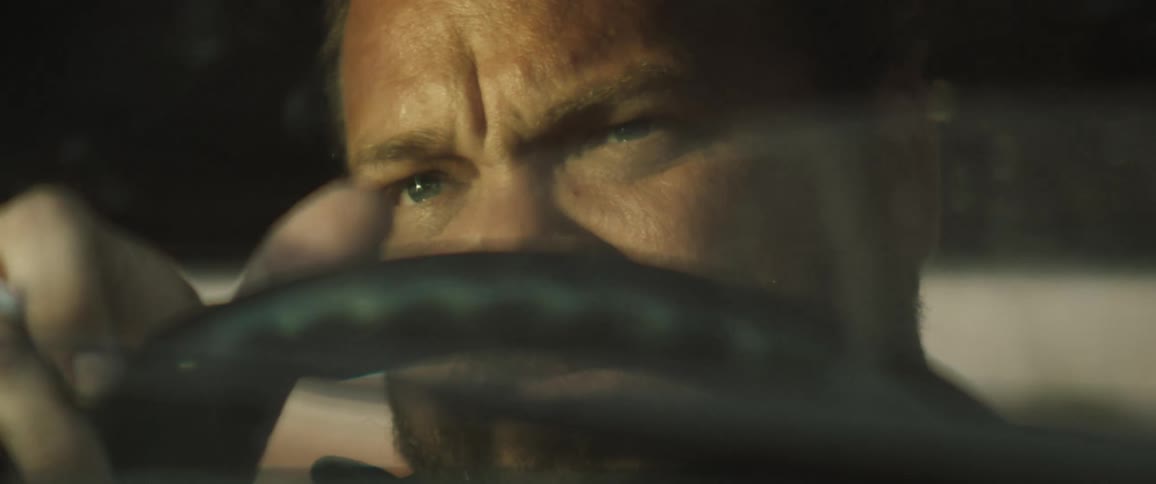A bearded man holds onto the steering wheel as he looks ahead