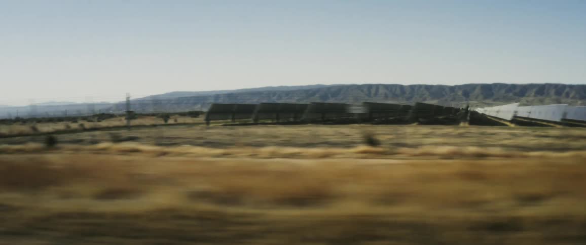 Sun reflecting from rows of solar panels on a solar farm in the desert with a mountain plateau in the background