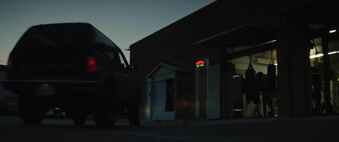 Vehicle drives past boxers training in gym near open doors at night