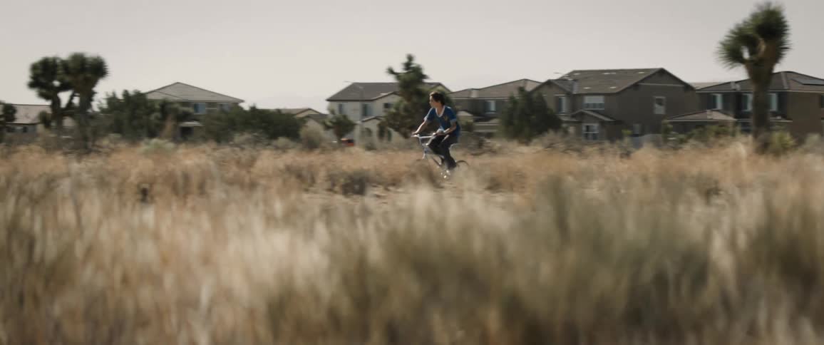 Cycling youth pedals past grassland near a residential neighborhood