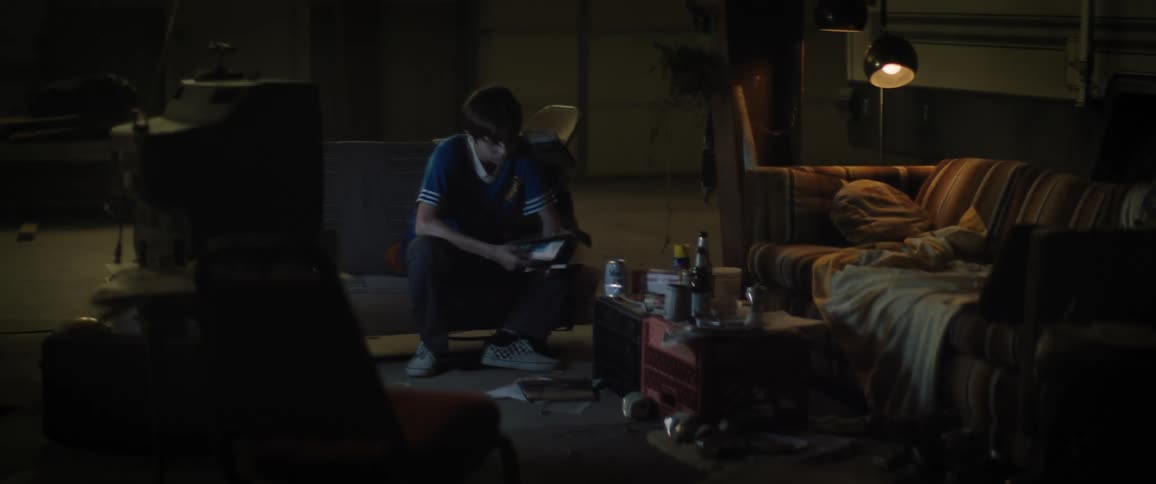 Young boy sitting in an armchair in a dimly lit room picking up a magazine that was on the floor