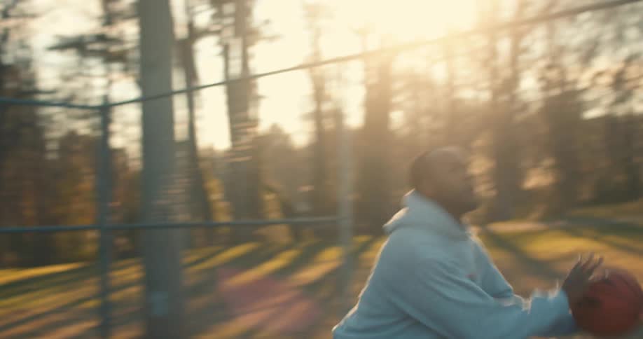 A person in a hoodie playing basketball in park at morning