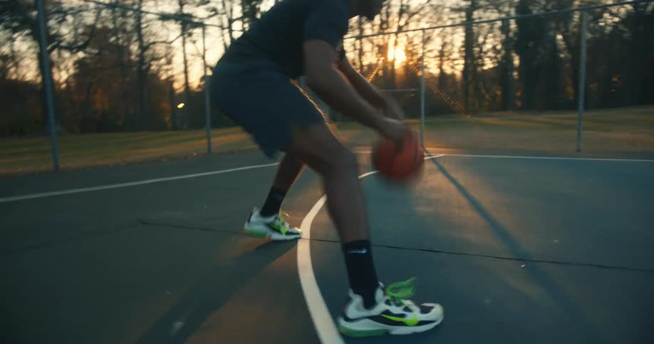 Basketball player dribbles ball back and forth on court during sunset