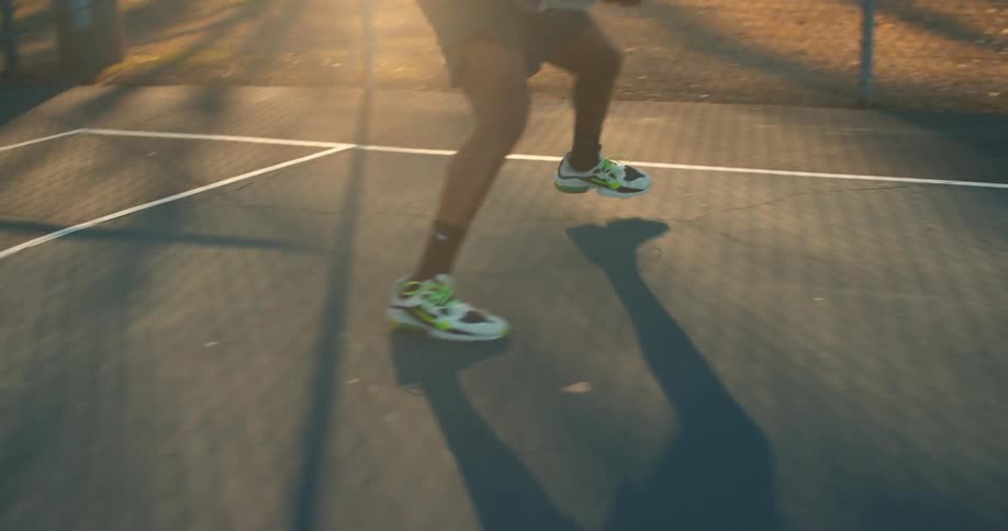 A person in a hoodie playing basketball in park at morning