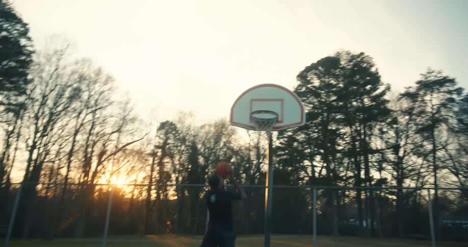 Man dribbling and playing basketball shooting the ball into the basket on an openair court