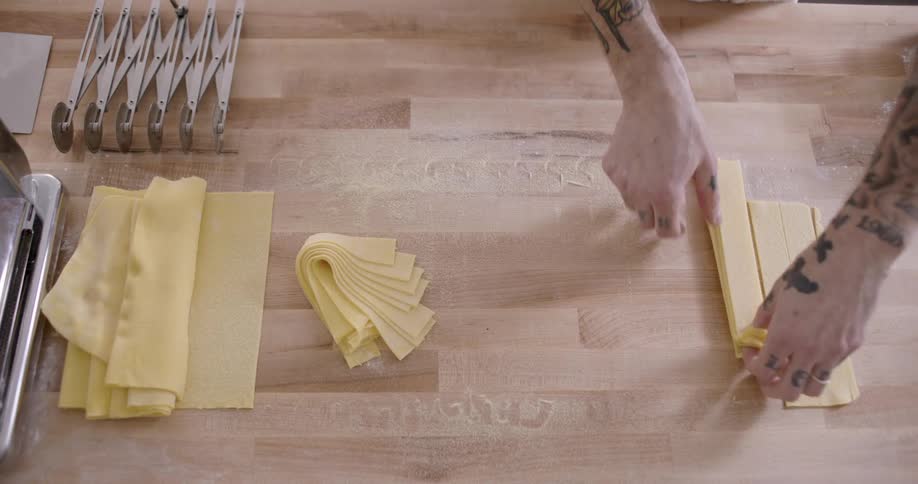 A person with tattoos is making pasta on a wooden countertop