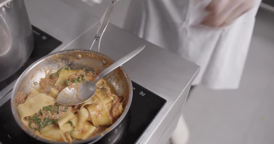 Closeup of a frying pan preparing pasta with chicken in sauce