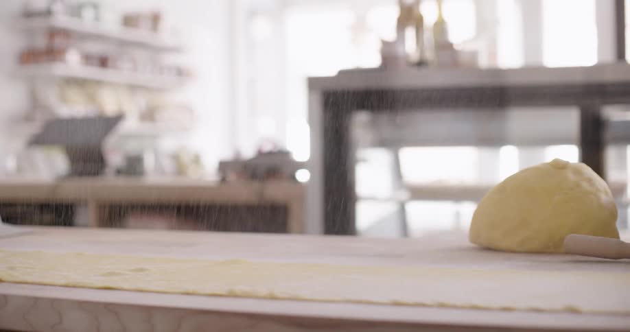 Hands of a man passing flour into a dough on a wooden countertop