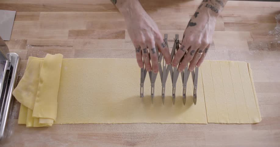 A persons hand using a tool to cut a piece of pasta that is opened in a table