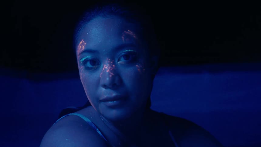 A portrait shot of a young Asian woman with pink face paint in a watery environment